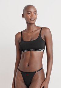 Svart bomullsbralette med tunna axelband och ett elastiskt midjeband med en vit logotyp. Matchas med en svart trosa.