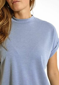 Ljusblå topp med kort ärm och rundad halsringning, tillverkad av mjukt material, med avslappnad passform och rullade ärmslut.