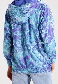 Hooded jacket in lightweight, glossy fabric with a blue and purple tie-dye pattern. Features elastic cuffs and hem, showcasing a relaxed fit.