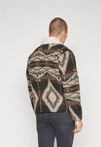 Gevoerde fleece jas met geometrische ontwerpen in bruin, crème en zwart, met een witte sherpa kraag en een relaxte pasvorm.