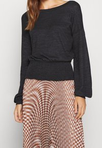 Black long-sleeve top with a gathered waistband, paired with a patterned brown and white skirt featuring wavy lines and geometric shapes.