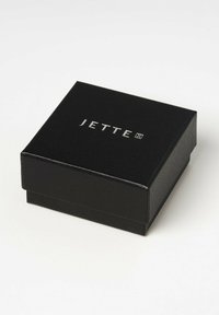 Scatola in similpelle nera con una superficie liscia. Presenta il logo argenteo "JETTE" sulla parte superiore. Forma quadrata, design minimalista.
