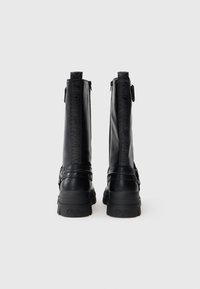 Čierne kožené členkové topánky s textúrovaným povrchom, vertikálnymi logovými detailmi a masívnou gumovou podrážkou. Obsahujú bočný zips pre jednoduché obúvanie.