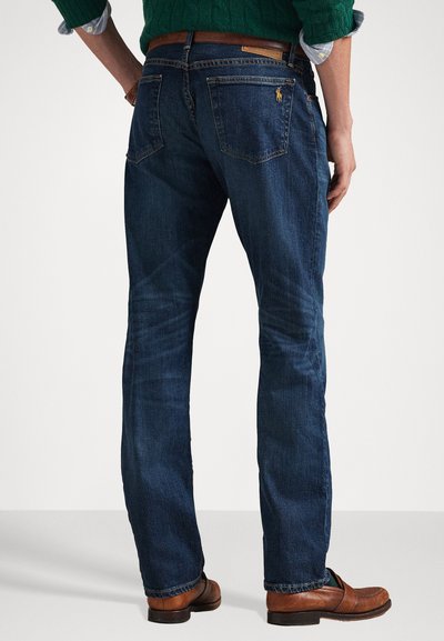 Dark blue denim jeans with a straight leg cut. Features back pockets with visible stitching and a small logo accent. Worn with a brown belt.