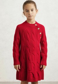 Crvena pletena haljina sa dugim rukavima, rebrastim izrezom i manžetama, sa tri zlatna dugmeta na ramenu.