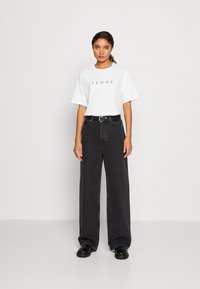 Witte kortarmige t-shirt met "FEMME" in het zwart gedrukt, gecombineerd met hoge, wijde zwarte jeans en zwarte schoenen.