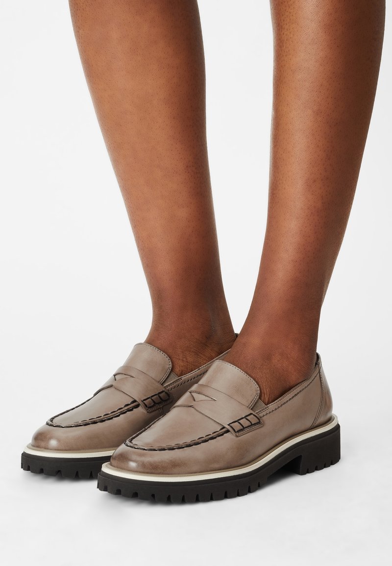 Mocassins en cuir gris avec une couture style mocassin, dotés d'une semelle extérieure noire épaisse et d'accents beiges autour de la semelle.