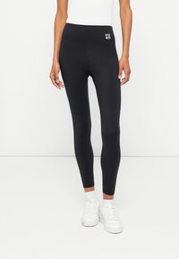 Svarta stretchiga leggings med hög midja som har en liten vit "HUGO"-logotyp. De har en slät yta och en kroppsnära design.