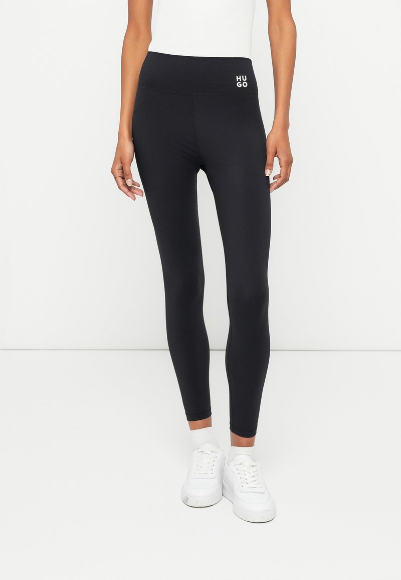 Svarta stretchiga leggings med hög midja som har en liten vit "HUGO"-logotyp. De har en slät yta och en kroppsnära design.
