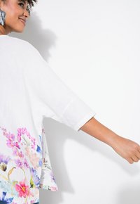 Top in lino bianco con una vivace stampa floreale nei toni del rosa, blu e viola. Maniche corte e vestibilità relaxed con orlo curvo.