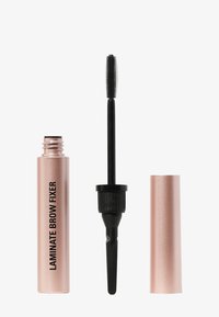 Un tubetto rosa oro etichettato "Laminated Brow Fixer" con un applicatore per mascara nero, allungato, accanto ad esso. Finitura metallica liscia, forma cilindrica.