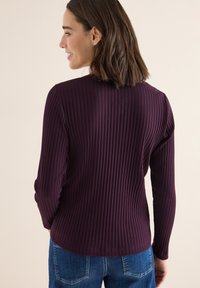 Bordeauxröd ribbad långärmad tröja med rund halsringning, som har en subtil textur och en figurnära design, tillsammans med blå denimjeans.