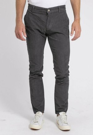 Pantalons en coton gris à coupe slim, avec poches latérales, fermeture à bouton et texture subtile. Associés à des baskets blanches.