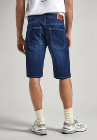 Shorts de mezclilla en azul oscuro con un corte recto, que cuentan con dos bolsillos traseros, costuras claras y una etiqueta de cuero en la cinturilla.