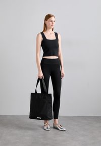 Top corto nero, leggings neri a vita alta, ballerine argentate e una borsa nera con tasca frontale e tracolla.
