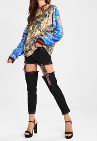 Färgglad oversized sweatshirt med blommönster och fåglar, kombinerad med svarta jeans i denim med utskärningar och remmar, samt högklackade sandaler.