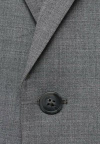 Tissu gris texturé avec un gros plan d'un bouton noir à quatre trous, mis en valeur sur le motif de tissage du matériau.