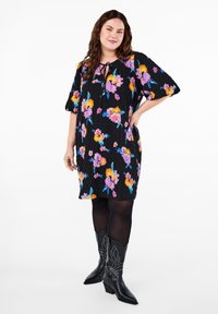 Kort svart klänning med färgglad blommönster, med korta ärmar och knytning vid halsen. Bärs med svarta, nitar prydda boots i westernstil.