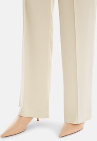 Cream wide-leg trousers with a smooth texture and a subtle sheen, paired with pointed nude heels featuring a stiletto heel.