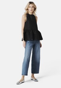 Černý peplum top s texturovanou tkaninou, spárovaný s modrými džíny se přímým střihem a stříbrnými plochými botami. Jednoduchý výstřih a vrstvený design.