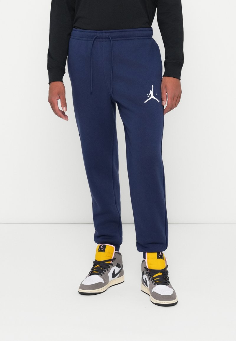 Tumši zilie sporta bikses no mīksta auduma, ar elastīgu jostu, aukliņu un baltu Jumpman logotipu kreisajā kājā.