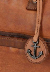 Braune Ledertasche mit glatter Textur, ausgestattet mit einem dunklen Metall-Ankeranhänger als Reißverschluss-Zug und kontrastierenden Nähten entlang der Kanten.