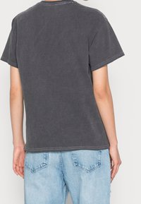 Grå bomullströja med avslappnad passform, korta ärmar och kontrasterande sömmar vid halsen. Tillsammans med ljusblå denim jeans.