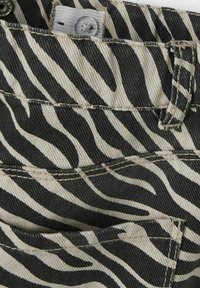 Tejido de denim con estampado de cebra en negro y crema, con costuras visibles, cierre de botón y detalles en los bolsillos.