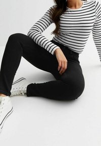 Jeans negros de corte ajustado, combinados con una camiseta de manga larga blanca y negra a rayas. Zapatillas altas blancas completan el look.