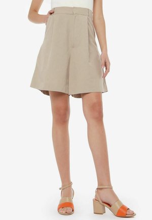Pantaloni shorts alti color beige chiaro con pieghe, realizzati in tessuto morbido. Abbinati a sandali con tacco a blocco color beige e arancione.