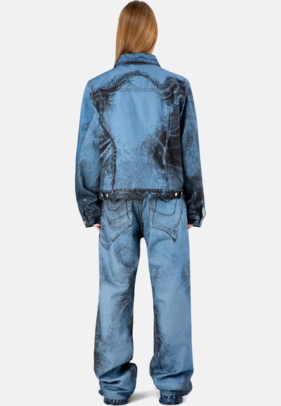 Completo in denim leggero blu chiaro con motivo spazzolato nero, caratterizzato da spalle ampie, tasche a toppa e orli sfrangiati.