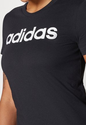 Zwart T-shirt met korte mouwen en wit "adidas"-logo gedragen door een persoon met een zichtbare tatoeage op de linkerarm.