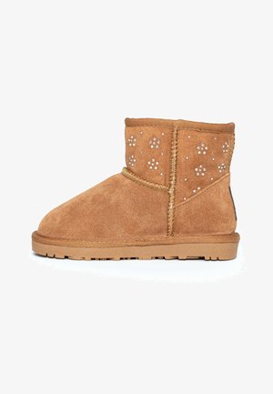 Stivaletti alla caviglia in suede tan con borchie decorative, dettagli cuciti, texture morbida e suola piatta in gomma. Punta tonda classica e design di altezza media.