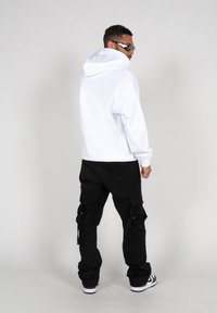 Hvid hættetrøje, sorte cargo-bukser med sidelommer og sportssko. Modellen ses fra bagpå, hvilket fremhæver en afslappet streetwear stil.