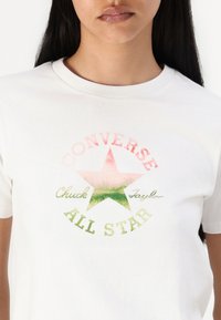 T-shirt bianca in cotone con una stampa grafica colorata di una stella e la scritta "Converse Chuck Taylor All Star" in rosa e verde.
