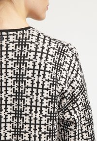 Pull en noir et blanc à motif, présentant un design géométrique, une texture tricotée et un détail de bouton à l'arrière du cou.