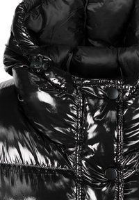 Nahaufnahme einer glänzenden schwarzen Daunenjacke, die den gepolsterten Kragen mit Druckknöpfen und einem verstellbaren Zugband zeigt.