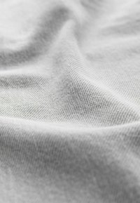 Tissu gris clair avec une texture lisse, présentant des motifs de tricot fins et réguliers ainsi que de légères ondulations dues au drapé.