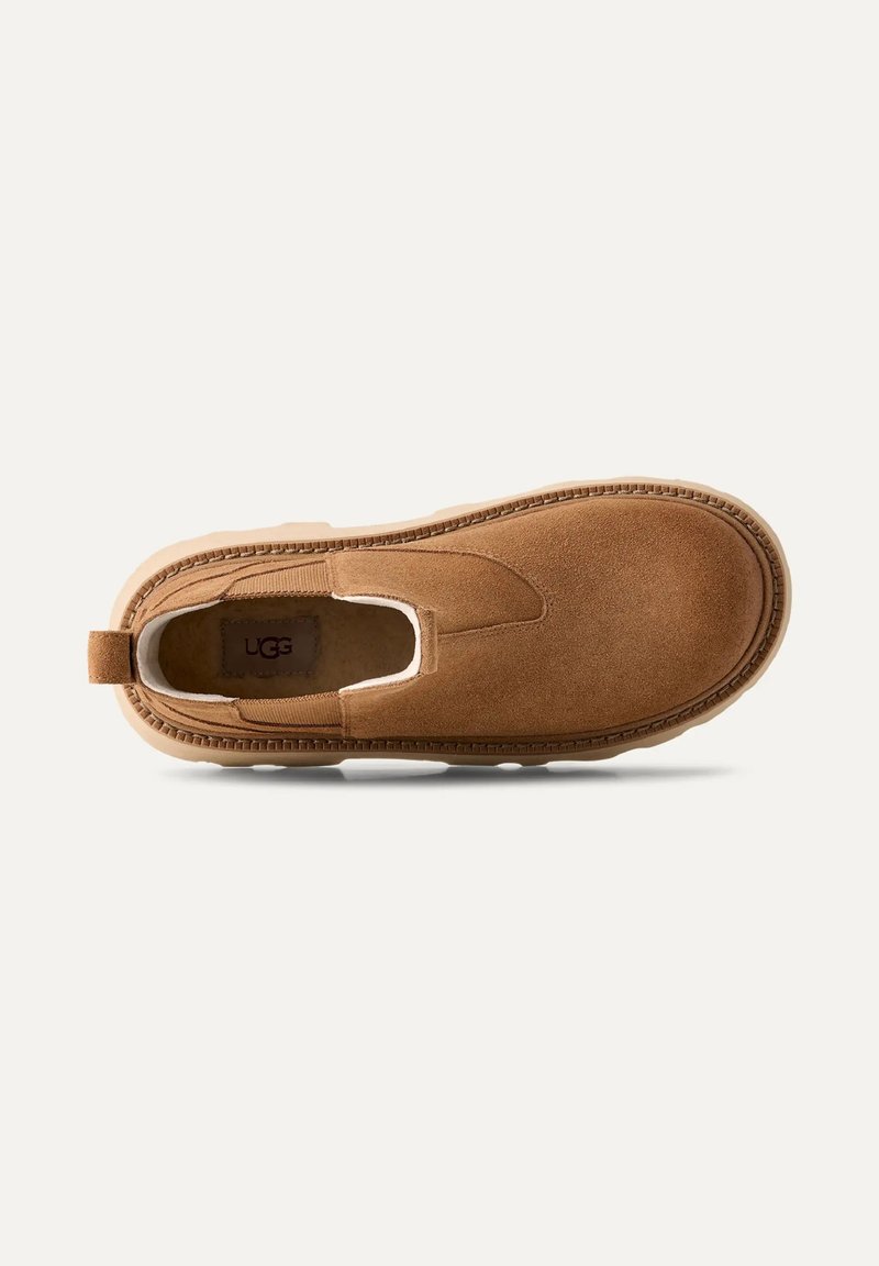 Brune ruskinds slip-on sko med elastiske sidelapper, rund tå og syet detaljering langs ydersålen. Brandlogo synligt indeni.
