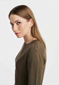 Oliwkowy sweter dziewiarski z okrągłym dekoltem, z trzema metalowymi guzikami na ramieniu i ściągaczami na mankietach.