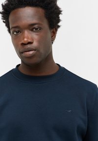 Sweatshirt bleu marine avec un col rond, fabriqué en tissu doux, présentant un logo brodé subtil sur la poitrine et une texture lisse.