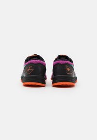 Zapatillas de correr negras con un material texturizado, acentos morados y una suela naranja. Incluye un logo y un patrón único en el talón.