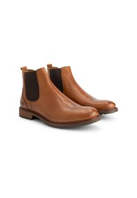 Een paar bruine leren Chelsea boots met donkere elastische zijpanelen en lage gestapelde hakken op een witte achtergrond.
