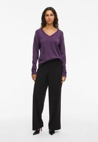Maglione viola a scollo a V con maniche lunghe, abbinato a pantaloni neri a gamba larga a vita alta e décolleté nere con punta. 