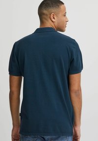 Polo bleu marine à manches courtes et col plat. Fabriqué en tissu lisse, avec des détails de couture subtils sur les épaules.