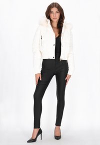 Afkortet hvid dunjakke med en faux pels hætte, blank tekstur, lynlåslommer og ribbede manchetter, kombineret med sorte tætsiddende bukser og hæle.