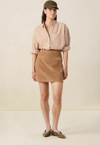 Jupe mini en velours côtelé marron avec deux poches avant, associée à une chemise oversized rayée dans des tons doux et une casquette à imprimé léopard.