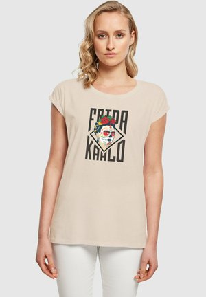 Beige bomulds T-shirt med korte ærmer, prydet med et Frida Kahlo grafik i livlige farver og fed sort skrift. Enkel, afslappet pasform.