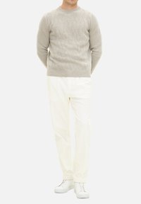 Lichtgrijze gebreide trui met een ruitpatroon, gecombineerd met witte broeken en witte sneakers. De outfit heeft een ronde halslijn en geribbelde manchetten.