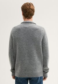 Grau gestrickter Pullover mit Schalkragen, ausgestattet mit strukturierter Oberfläche und langen Ärmeln, kombiniert mit blauen Jeans.